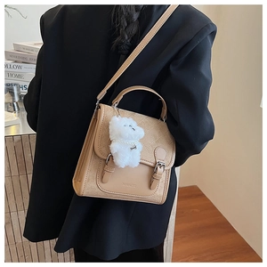 Stylish khaki crossbody bag with quilted flap and cute bear pendant on a black blazer