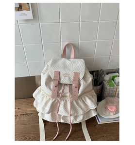 Detailed view of the ruffle hem and pink polka dot pattern on a white canvas backpack