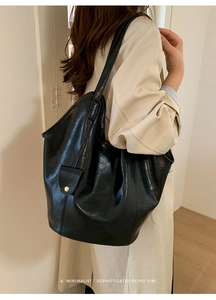 Détail d'un grand sac cabas en cuir noir brillant porté à l'épaule par un mannequin