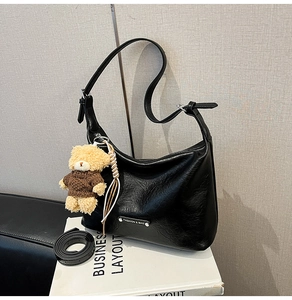Detail view of black hobo bag with silver logo tag, plush bear charm, and spare long strap