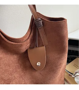 Détail d'un cabas vintage en daim marron avec anses en cuir et nœud décoratif violet