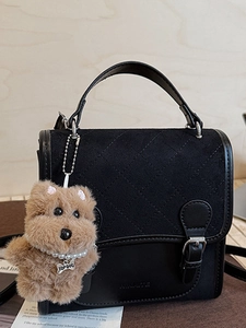 Quilted black satchel with flap and brown plush puppy charm on a wooden background