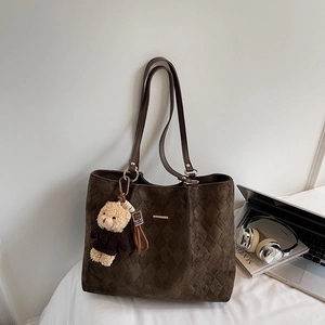 Close-up of quilted coffee tote bag with a cute bear charm and laptop for office commute