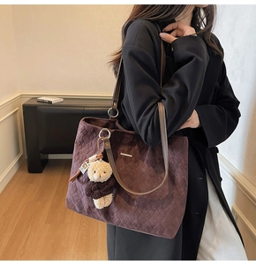 Detail of chocolate tote bag featuring woven texture and a cute beige teddy bear charm