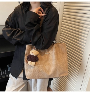 Detail of large khaki tote bag featuring quilted pattern and cute brown teddy bear charm