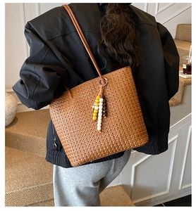 Detail of a brown woven tote bag with bead charms and slender shoulder strap shown on model