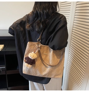 Beige quilted tote bag featuring a teddy bear charm shown on model in a cozy home setting