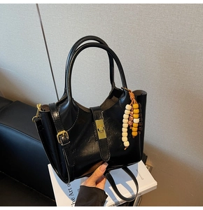 Detalle de bolso de mano en cuero brillante negro con cierre dorado y adorno de cuentas