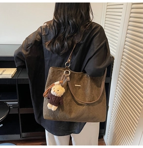 Detail of a large brown quilted tote bag with a plush bear charm on a female model
