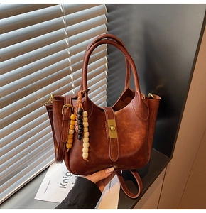 Detalle del bolso de cuero marrón con colgante de madera y cierre metálico dorado elegante