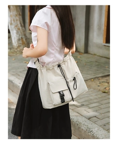 Close-up of drawstring bucket bag in cream nylon with black buckle pocket in outdoor street setting