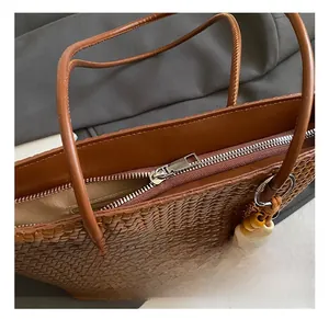 Detail shot of a brown woven tote bag featuring a silver metal zipper and beaded charm