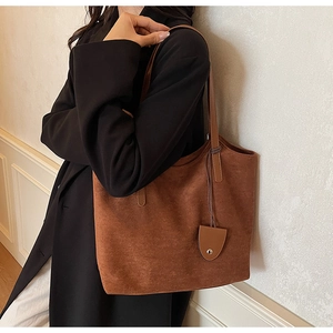Gros plan d'un sac cabas marron en daim avec surpiqûres et pendentif métallique