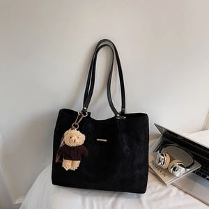 Detail of black quilted tote bag with gold metal trim and a cute teddy bear pendant