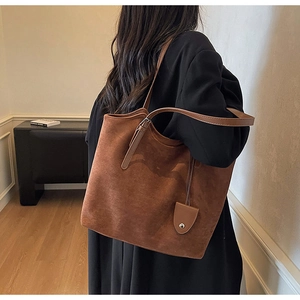 Détail d'un grand sac cabas en daim marron avec de fines bandoulières et un accessoire