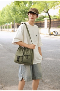 Outdoor street view of olive green canvas drawstring bucket bag with adjustable wide strap