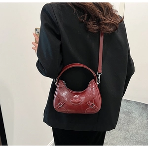 Detail of burgundy glossy leather handbag showing embossed logo and metal buckles