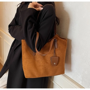Détail d'un sac cabas en daim marron avec bandoulières en cuir foncé sur un manteau noir