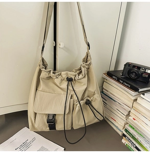 Detail of beige nylon drawstring bucket bag showing front pocket with black buckle closure