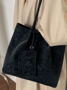 Minimalist black tote bag in matte leather finish shown on model in beige coat