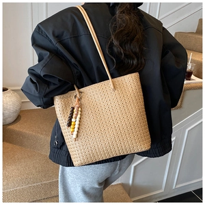 Close-up of beige woven tote bag with a wooden bead tassel charm on shoulder