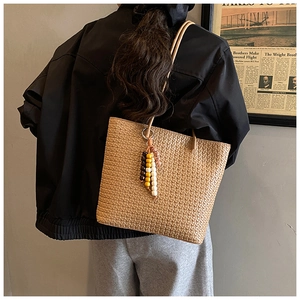 Detail of woven straw tote bag with colorful beaded charm and minimalist handle
