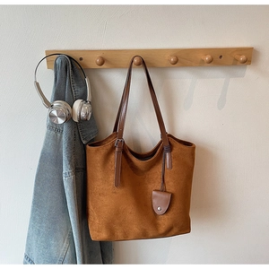 Gros plan d'un sac cabas en daim marron vintage avec anses en cuir sur un portant en bois