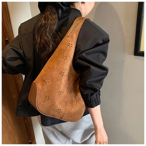 Detail of laser-cut flower patterns on brown suede hobo shoulder bag with wide strap