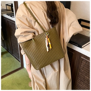 Detail of dark green woven tote bag with colorful beaded charm on a shoulder strap