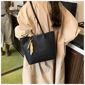 Close-up of black woven leather tote bag with unique ethnic wooden bead charm detail