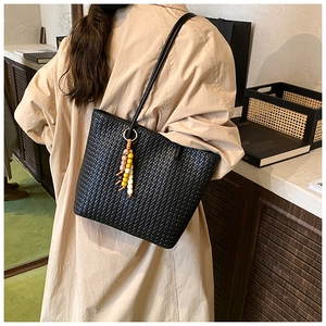 Detail of black woven tote bag with Intrecciato texture and decorative beaded keychain