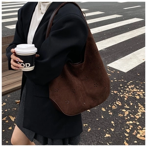 Detail of laser-cut floral pattern on dark brown suede bucket bag in street style setting