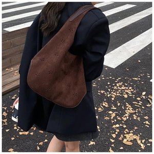 Detail of laser-cut floral patterns on a dark brown suede leather shoulder bag