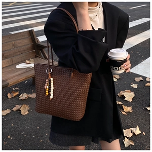 Detail shot of a dark brown woven tote bag with colorful beaded tassel in autumn city street