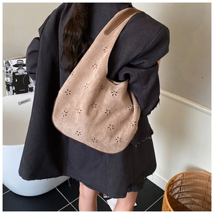 Close-up of a brown suede hobo bag with laser-cut floral patterns on a woman's shoulder