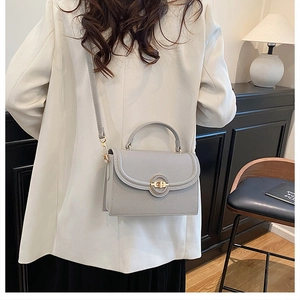 Model wearing a grey lychee leather crossbody bag with a round gold lock closure