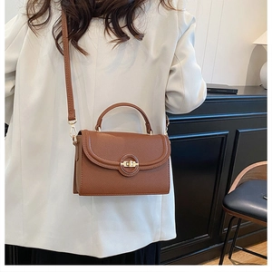 Close-up of brown litchi grain leather crossbody bag with elegant golden rotary lock