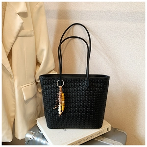 Close-up of black woven tote bag featuring a decorative beaded tassel and shoulder strap
