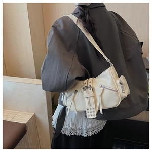 Close-up of off-white faux leather biker bag with multiple zippers on a gray suit outfit