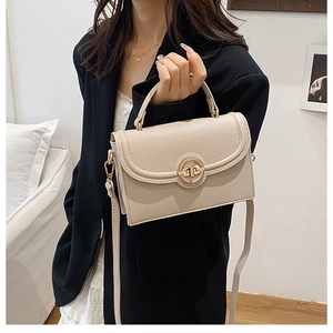 Detail of elegant beige crossbody bag with textured leather and gold circular buckle