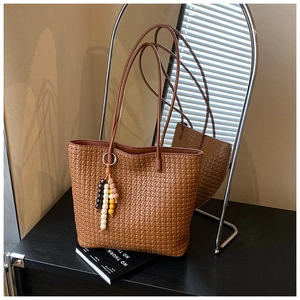 Close-up of brown woven tote bag with colorful beaded charm on an elegant surface