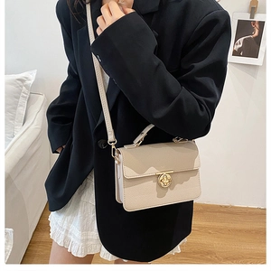 Detail of off-white leather handbag with golden floral twist lock on a black suit