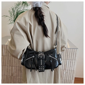 Detail view of black patent leather underarm bag featuring silver zippers and punk studs
