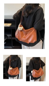 Detail view of brown dumpling shoulder bag with plush bear charm and chain strap detail