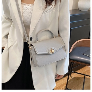 Detail of grey lychee textured leather handbag with gold metal clasp on white suit model
