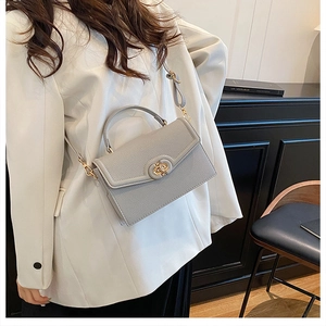 Detail view of grey pebble leather handbag with gold twist lock and shoulder strap worn by model