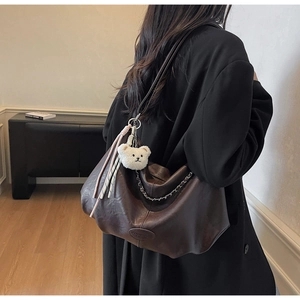 Detail of a large brown faux leather tote bag with silver chain and cute teddy bear charm