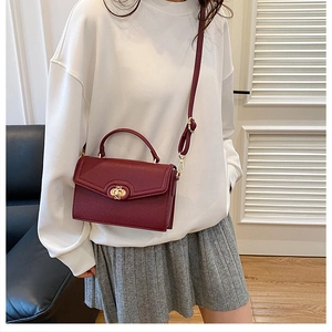 Detail view of burgundy pebble leather handbag with gold metal lock and top handle