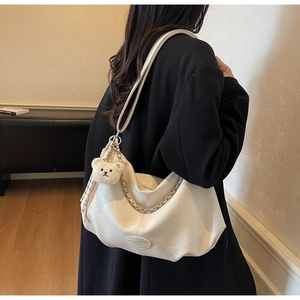 Chic beige leather dumpling bag with decorative chain and plush bear pendant detail