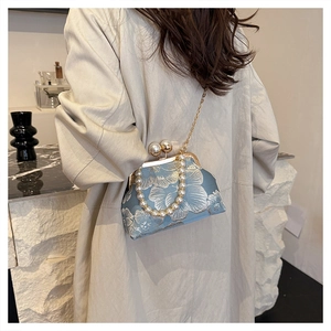 Elegant embroidered floral handbag with pearl handle worn by model in trench coat